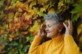 Senior woman standing outdoors against colorful natural autumn background, eyes closed.