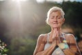 A senior woman standing outdoors on a terrace in summer, doing yoga.