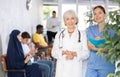 Senior woman standing with young female assistant in clinic lobby Royalty Free Stock Photo