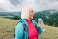 caucasian 50s blonde girl drinking water from plastic bottle. Mountain background