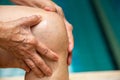 Senior woman suffering from knee pain, Massaging by her hand, Blue swimming pool Royalty Free Stock Photo