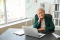 Senior woman suffering from neck pain while sitting at table with laptop Royalty Free Stock Photo