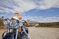 Senior woman in sunglasses poses on motorcycle on desert road