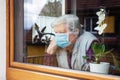 Senior woman with surgical mask sitting on a window at home, coronavirus and covid-19 provisions Royalty Free Stock Photo