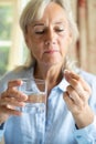 Senior Woman Taking Tablet With Glass Of Water At Home