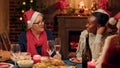 Senior woman talking with festive young adult person while enjoying Christmas dinner at home. Royalty Free Stock Photo