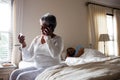 Senior woman talking on mobile phone while looking at medicine in bedroom Royalty Free Stock Photo