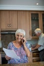 Senior woman talking on mobile phone while man working in kitchen Royalty Free Stock Photo