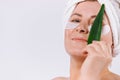 Senior woman with a towel on her head covering her eyes with a leaf of aloe vera on a white background with empty side