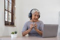 Senior woman using laptop while wearing headphones at home - Joyful elderly lifestyle and technology concept Royalty Free Stock Photo