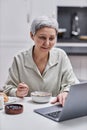 Senior woman using laptop and working while enjoying breakfast at home Royalty Free Stock Photo