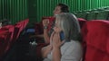 Senior woman using mobile phones in movie theater disturbs other audiences.