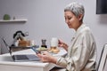 Senior woman using smartphone and working while enjoying breakfast in morning Royalty Free Stock Photo