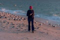 Senior woman walking on beach with birds following her.