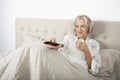 Senior woman watching TV while having coffee in bed Royalty Free Stock Photo