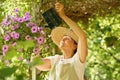 Senior woman waters flowers in a hanging pot