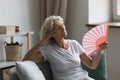 Senior woman waving fan feels unwell due unbearable hot weather