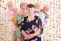 Senior woman wearing elegant blouse standing in front of group of senior happy fiends looking from behind her