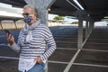 A senior woman wearing flowered medical mask standing in a deserted parking looking at smart phone