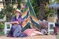 Senior woman wearing a hat holding a ukulele and looking at the camera while sitting on a chair in a garden with Bohemian style of