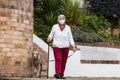 Senior woman wearing a home made face mask and having a short walk outdoors with her pet during the coronavirus quarantine de-