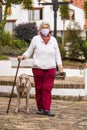 Senior woman wearing a home made face mask and having a short walk outdoors with her pet during the coronavirus quarantine de-