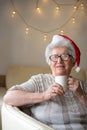 Senior woman wearing red Santa's hat enjoying cup of tea at warm home. Xmas, senior, age concept Royalty Free Stock Photo