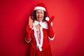 Senior woman wearing Santa Claus costume holding christmas gift over isolated red background very happy and excited, winner Royalty Free Stock Photo