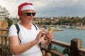 Senior woman wearing santa claus hat on Antalya old city background getting directions using online maps on your phone, new year