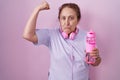 Senior woman wearing sportswear and headphones strong person showing arm muscle, confident and proud of power