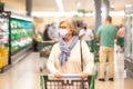 Senior woman wearing a surgical mask due to the coronavirus pushes a shopping cart in the grocery department of a supermarket