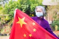 Senior woman wearing a surgical mask and holding the China flag for giving encouragement to the Chinese to fight covid-19