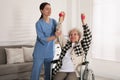 Senior woman in wheelchair doing physical exercise and young caregiver helping her indoors. Home health care service Royalty Free Stock Photo