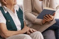 Senior woman and helpful volunteer at nursing home reading book together Royalty Free Stock Photo