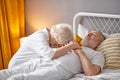 Senior woman sitting next to dying husband lying on bed and crying