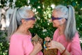 Senior women twins in colourful clothes with extraordinary handbags in city, talking and smiling.