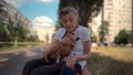 Senior 90-year-old woman with gray hair and deep wrinkles sits outdoors In assisted living facility on bench with small Royalty Free Stock Photo