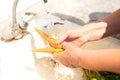 Seniors hands wash ripe new crop carrots under a tap of warm water on the streets of the garden on a sunny summer day. Royalty Free Stock Photo