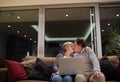 Seniors with laptop sitting on a couch, kissing Royalty Free Stock Photo