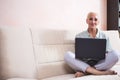 Seniors and Technologies Concepts. Smiling Relaxing Caucasian Senior Woman Posing With Laptop And Listening To The Music on Couch