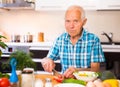 senor man preparing fresh vegetable salad at home in the kitchen Royalty Free Stock Photo