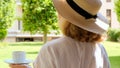 Senora female, age 50-55 in a straw hat holds a cup of hot drink and drinks coffee, sitting in the morning on a summer Royalty Free Stock Photo