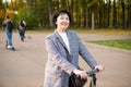 A senora in her 50s on a scooter in casual clothes enjoys life on a walk in the park. Active lifestyle in middle aged, sports.