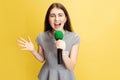 Half-length portrait of young girl, correspondent holding reporter microphone isolated on yellow studio background