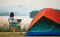 A sense of peace and serenity photo of female traveler sitting beside camping tent and using notebook laptop computer working from