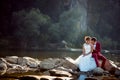 Sensitive portrait of the groom in red suit kissing the adorable bride in the shoulder while sitting on the stone near Royalty Free Stock Photo