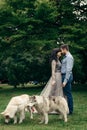 Sensitive portrait of the happy elegant charming couple rubbing noses during their walk with two huskies in the park Royalty Free Stock Photo