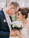 Sensitive portrait of the just married standing head-to-head while holding the wed bouquet. Royalty Free Stock Photo