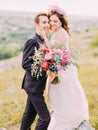 Sensitive portrait of the smiling hugging newlyweds holding the huge wedding bouquet.