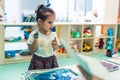 Sensory play for early brain development at nursery school. Toddler little girl milk painting with her fingers, using Royalty Free Stock Photo